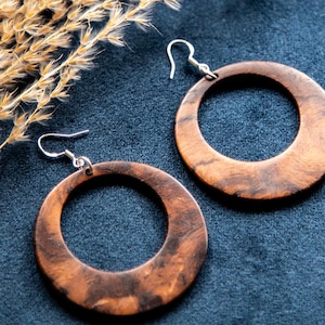 May include: A pair of large, round wooden earrings with a brown and black marbled pattern. The earrings have silver hooks.