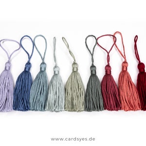 May include: Ten colorful tassel ornaments in shades of purple, blue, green, red, and orange. The tassels are made of soft yarn and have a loop at the top for hanging.