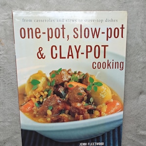 May include: A cookbook titled "one-pot, slow-pot & CLAY-POT cooking" by Jenni Fleetwood. The cover features a close-up of a stew with meat, vegetables, and herbs in a white bowl. The title is in large, bold, red and white letters.