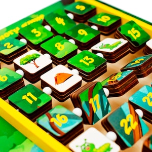 Pode incluir: Um jogo de mem&oacute;ria de madeira com pe&ccedil;as verdes e azuis que mostram os n&uacute;meros de 1 a 24. Cada pe&ccedil;a tem uma imagem diferente de uma &aacute;rvore, uma tenda ou uma lagarta. O jogo &eacute; projetado para ajudar as crian&ccedil;as a aprender os n&uacute;meros e as habilidades de mem&oacute;ria.