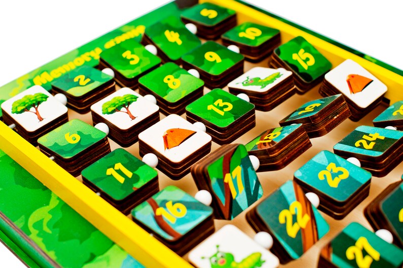 Pode incluir: Um jogo de mem&oacute;ria de madeira com pe&ccedil;as verdes e azuis que mostram os n&uacute;meros de 1 a 24. Cada pe&ccedil;a tem uma imagem diferente de uma &aacute;rvore, uma tenda ou uma lagarta. O jogo &eacute; projetado para ajudar as crian&ccedil;as a aprender os n&uacute;meros e as habilidades de mem&oacute;ria.