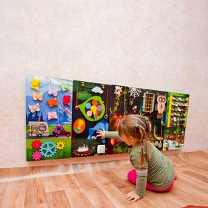 Pode incluir: Um painel de atividades de madeira colorido com v&aacute;rias texturas e atividades para crian&ccedil;as. O painel apresenta um tema de borboleta, uma cena de floresta e uma cena de fazenda. Uma crian&ccedil;a pequena est&aacute; interagindo com o painel, tocando uma aba azul.