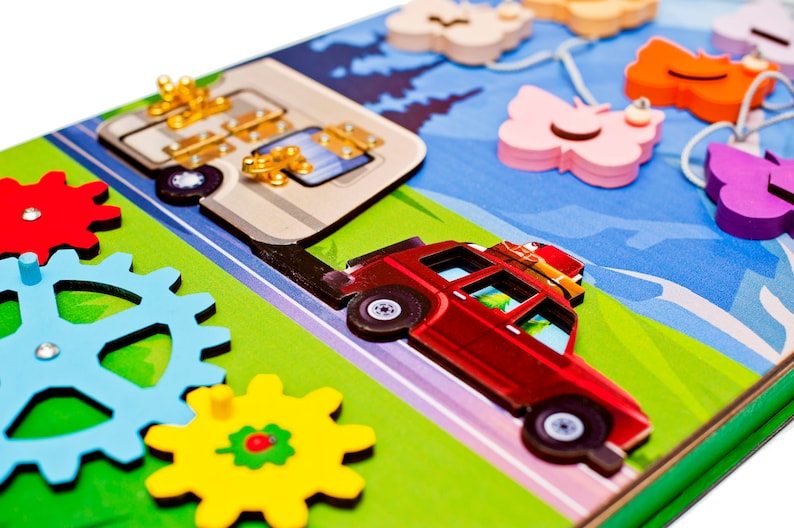 Pode incluir: Um brinquedo de madeira com um carro vermelho, um autocaravana e engrenagens. O carro tem um porta-bagagens no telhado com bagagem no topo. A autocaravana tem uma porta com uma trava. As engrenagens s&atilde;o azuis, amarelas e vermelhas. O fundo &eacute; verde e azul.