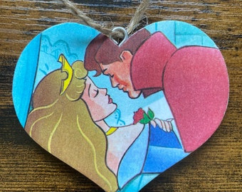 Könnte beinhalten: Ein herzförmiger Anhänger mit einem Bild von einem Prinzen und einer Prinzessin, die sich küssen. Der Anhänger ist aus Holz und hat eine Juteschnur zum Aufhängen.