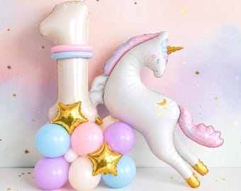 May include: A balloon arrangement featuring a large beige number one balloon, a white unicorn balloon with a pastel mane and gold horn, and a base of small blue, pink, and purple balloons accented with shiny gold star-shaped foil balloons.
