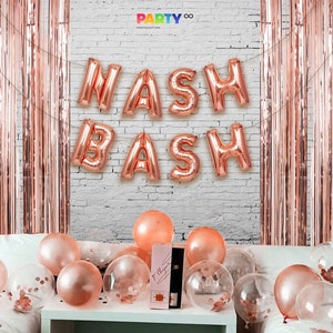 May include: Rose gold foil fringe curtains with rose gold letter balloons spelling "NASH BASH" on a white brick wall. There are rose gold and clear balloons with confetti on a white table in front of the wall.