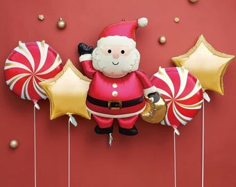 May include: A collection of foil balloons featuring a central Santa Claus figure, two round red and white peppermint swirl balloons, and two gold star-shaped balloons. The Santa balloon wears a red suit with a black belt and holds a gold sack.