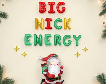 May include: Foil balloons spelling BIG NICK ENERGY in red, gold, and green. Below the text is a Santa Claus foil balloon wearing a red suit and hat, carrying a green gift. The arrangement is framed by green pine branches and small gold stars.