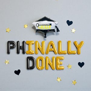 May include: A graduation-themed balloon arrangement. The phrase "PHINALLY DONE" is spelled out with black and gold letter balloons. A graduation cap balloon and star and heart-shaped decorations complete the celebratory scene.