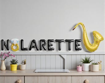 May include: A decorative display featuring black balloon letters spelling "NOLARETTE" with a diamond ring balloon and a gold saxophone balloon. The display is set above a wooden cabinet with plants and a candle.