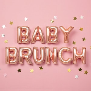 May include: Rose gold foil balloons spelling out "BABY BRUNCH" on a pink background, scattered with gold and silver star-shaped confetti. A festive and celebratory theme.