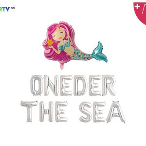 Op de afbeelding: Een ballon in de vorm van een zeemeermin met roze haar en een turquoise staart, die een gele vis vasthoudt. Zilverkleurige folieballonnen met de tekst "ONEDER THE SEA". Inclusief een rietje en een touwtje voor de ballon. Feestdecoratie voor een eerste verjaardag.