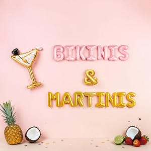 May include: Pink and gold foil balloons spelling "BIKINIS & MARTINIS" on a pink background. A gold martini glass balloon and tropical fruit, including pineapple, coconut, and strawberries, complete the scene.