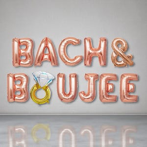 May include: Rose gold foil balloons spelling out "BACH & BOUJEE" with a diamond ring balloon. The balloons are displayed against a gray wall, perfect for a bachelorette party or bridal shower.