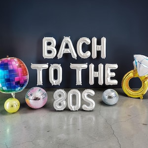 Op de afbeelding: Een verzameling feestballonnen met de tekst "BACH TO THE 80S". Inclusief een discobal, een diamantringballon en twee kleinere discobalballonnen. De discobal heeft een regenboogkleurenschema.