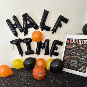 May include: A festive birthday scene with black "HALF TIME" balloon letters, orange and yellow balloons, and a basketball. A sign reads "ZAAHIR my 1/2 birthday" with details about the child's likes and dislikes.