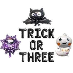 May include: A collection of Halloween-themed foil balloons. Includes a black bat, a purple spider in a web, a white ghost with orange cheeks, and black letter balloons spelling "TRICK OR THREE".