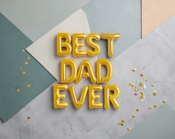 Puede incluir: Letras doradas de globo de papel de aluminio que deletrean "BEST DAD EVER" sobre un fondo geométrico gris, azul y beige. Confeti dorado disperso añade un toque festivo, perfecto para el Día del Padre o un cumpleaños.