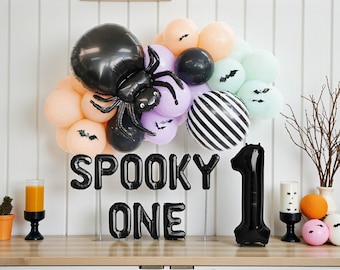 May include: A Halloween-themed party decoration featuring a black spider balloon, a cluster of pastel balloons, and a black and white striped balloon. The phrase "SPOOKY ONE" is spelled out in black balloon letters, with a large black number 1 balloon.