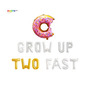 May include: A pink and gold donut-shaped balloon with a bite taken out of it, and the phrase "GROW UP TWO FAST" spelled out in silver and gold foil balloons. Party decor.