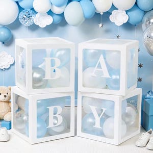 May include: White square boxes spelling "BABY" with clear sides, filled with blue and white balloons. The boxes are decorated with white letters. The background features blue and white balloons, a teddy bear, and baby shoes.