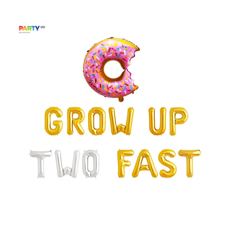 May include: A pink and gold donut-shaped balloon with sprinkles, with a bite taken out of it, above gold and silver letter balloons spelling "GROW UP TWO FAST". Party decorations for a birthday celebration.