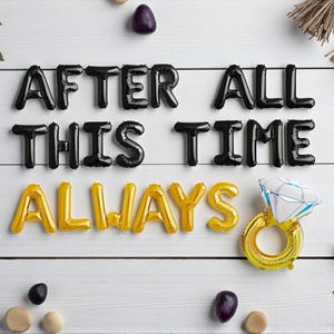 May include: A white wooden surface displays black and gold foil balloons spelling "AFTER ALL THIS TIME ALWAYS". A gold ring balloon with a diamond-shaped gem is also present, along with decorative elements.
