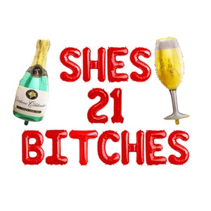 May include: A collection of red foil balloons spelling out "SHES 21 BITCHES" with a champagne bottle and a champagne glass balloon. The champagne bottle is green and gold, and the glass is yellow and silver.