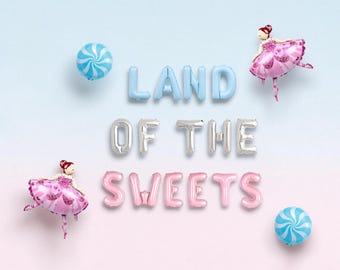 May include: Foil balloons spelling LAND OF THE SWEETS in light blue, silver, and pink. Two pink-clad ballerina balloons and two blue and white swirl candy balloons are arranged around the text on a light blue and pink gradient background.