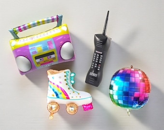 Könnte beinhalten: Ein Set aus vier Folienballons, bestehend aus einem gelb-violetten Ghettoblaster, einem schwarzen Mobiltelefon, einem weißen Rollschuh mit Regenbogenstreifen und goldenen Rollen sowie einer bunten Discokugel mit quadratischem Muster.