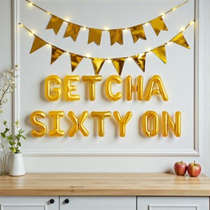 May include: A festive wall decoration for a 60th birthday celebration. Gold foil balloon letters spell out "GETCHA SIXTY ON" below a gold banner and string lights. Two red apples sit on a wooden counter.