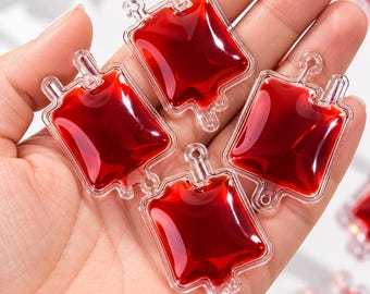 May include: Four clear acrylic charms shaped like blood bags filled with a deep red liquid. Each charm features a rectangular body with a small loop at the top for hanging and a small nozzle detail at the bottom, mimicking a medical IV bag.