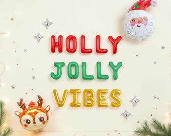 May include: A set of foil balloons spelling HOLLY JOLLY VIBES in red, green, and gold. The display includes a Santa Claus head balloon, a reindeer head balloon, and several small silver star-shaped balloons arranged on a light background.