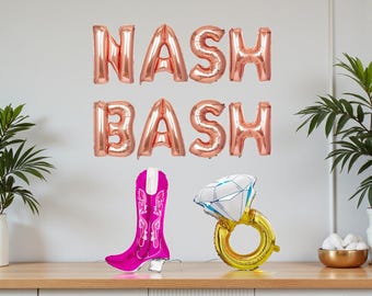 May include: A rose gold "NASH BASH" balloon banner hangs above a pink cowboy boot and a diamond ring balloon. The boot has white accents and a light-up base. The ring is gold with a white and blue diamond.
