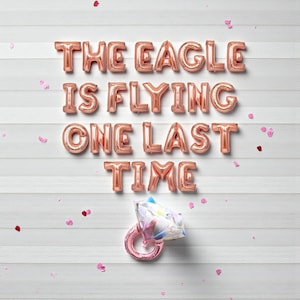 Puede incluir: Letras de globo de papel de aluminio en oro rosa deletrean "THE EAGLE IS FLYING ONE LAST TIME" sobre un fondo blanco de paneles de madera. Un globo de anillo de oro rosa con una gema en forma de diamante está en la parte inferior. Confeti rosa esparcido.