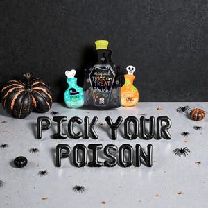 May include: A Halloween-themed still life featuring decorative bottles with labels like "Magical Trick or Treat Potion" and "Zombie Tonic." Black balloon letters spell "Pick Your Poison." Pumpkins and spiders complete the spooky scene.