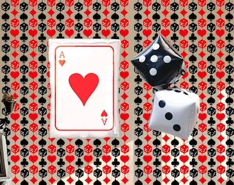 May include: A decorative wall with a repeating pattern of playing card suits and dice. A large Ace of Hearts card and two inflatable dice, one black and one white, are suspended in front of the wall. The Ace of Hearts card has a red heart in the center.
