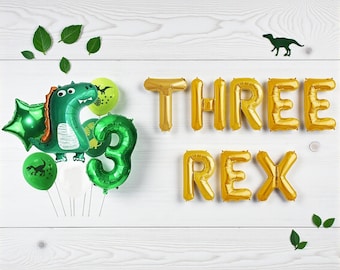 May include: A festive birthday scene with green dinosaur and number 3 balloons, along with gold foil balloons spelling "THREE REX." Green balloons with dinosaur silhouettes and green leaves are scattered on a white wooden background.