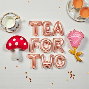 May include: A festive arrangement for a tea party, featuring rose gold foil balloons spelling "TEA FOR TWO". Includes a red mushroom balloon, a pink rose balloon, two teacups, and a teacup with saucer. Gold star confetti is scattered around the scene.