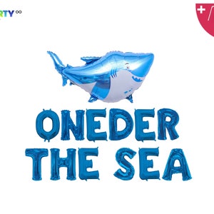 May include: A blue shark-shaped balloon and blue foil letter balloons spelling "ONEDER THE SEA" against a white background. The shark balloon has white accents and a smiling face. PartyEight.com logo is in the top left corner.