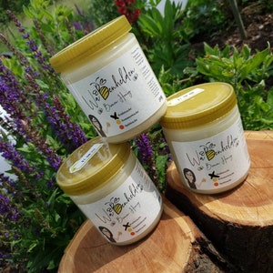 Könnte beinhalten: Drei Honiggläser mit goldenen Deckeln. Die Gläser sind mit "Wabenheldin" und "Bienen Honig" beschriftet. Die Gläser stehen auf einer Holzoberfläche.