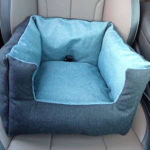 Könnte beinhalten: Ein blaues und schwarzes Haustierbett für das Auto. Das Bett hat eine weiche, blaue Stoffauskleidung und eine schwarze Außenhülle. Das Bett ist so konzipiert, dass es in den Rücksitz eines Autos passt.