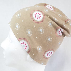 Könnte beinhalten: Eine beige Mütze mit einem weißen und rosafarbenen geometrischen Muster. Die Mütze hat eine lockere Passform und ist aus einem weichen, bequemen Stoff gefertigt.