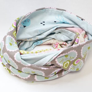 Könnte beinhalten: Ein grauer, blauer und rosa Infinity-Schal mit einem Blumenmuster. Der Schal ist aus weichem Stoff und perfekt, um sich im Winter warm zu halten.