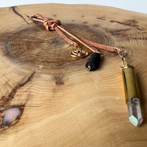 May include: A brown leather cord necklace with a gold charm, a black lava rock bead, and a gold-capped clear quartz crystal pendant.