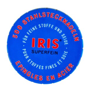 Peut inclure: Une bo&icirc;te ronde bleue avec des inscriptions blanches qui disent "500 Stahlstecknadeln" et "Iris Superfein" en rouge. La bo&icirc;te est pour des aiguilles &agrave; coudre.