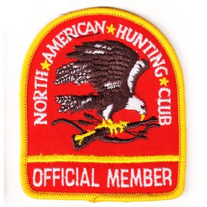 May include: Embroidered patch with a red background and a yellow border. The patch features a brown and white eagle perched on a branch. Text includes "NORTH AMERICAN HUNTING CLUB" and "OFFICIAL MEMBER".
