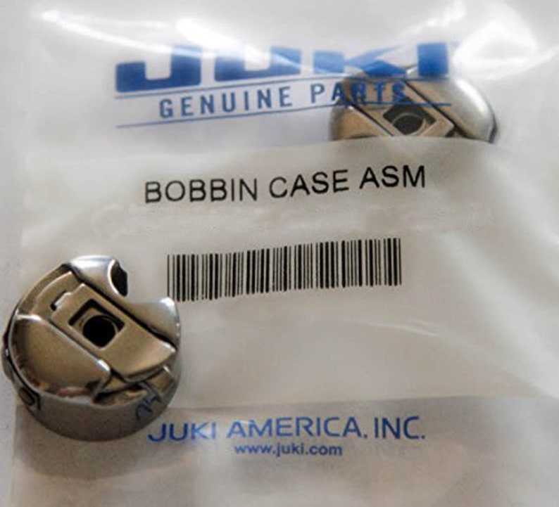 Puede incluir: Un ensamblaje de caja de bobina de plata para una m&aacute;quina de coser. El empaque incluye el logotipo de Juki Genuine Parts y el texto "Bobbin Case ASM".