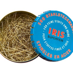 May include: A blue tin with a white and red label containing 500 steel sewing pins. The label reads "500 Stahlstecknadeln für feine Stoffe und Seide - Iris Superfein - Epingles en acier pour étoffes fines et soie".