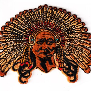 May include: Embroidered patch of a Native American chief wearing a headdress with feathers in shades of brown, black, and red. The chief has a serious expression and turquoise colored earrings.